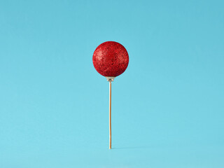 Lollipop made of red Christmas bauble on blue background. Christmas sweets concept