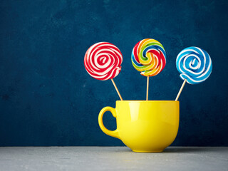 Colorful lollipops in yellow coffee cup against blue textured background. Abstract food art