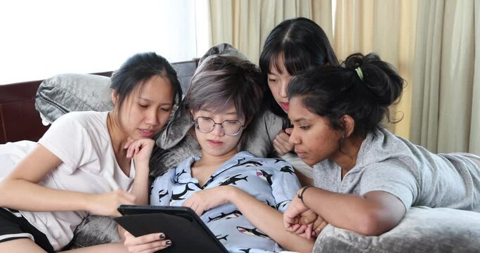 Young Asian girls sleepover pajama party studay red play game on tab on large bed in bedroom with bright light window
