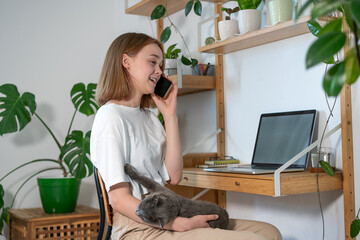 Young woman freelancer working on laptop at home in modern room with plants. Girl using a computer for study online at home, female user busy on a distance internet job. Cozy office workplace, remote
