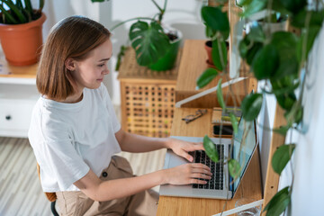 Young woman entrepreneur working on laptop at home. Freelancer typing email on a laptop, girl using a computer for study online at home, female user busy on a distance internet job. Remote online work