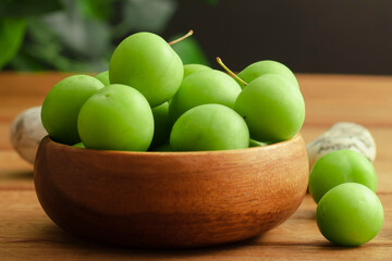 green plum in wooden bamboo bowl and black background