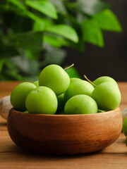 green plum in wooden bamboo bowl and black background
