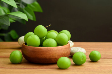 green plum in wooden bamboo bowl and black background