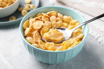 Spoon in bowl with tasty cornflakes and milk on light grey table