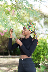 Beautiful African girl dressed in black standing in the garden looking intently at the leaves of a...