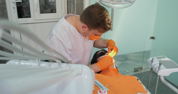 female patient at dentist appointment lies in chair during dental treatment at professional stomatologist, medical man in sterile gloves and mask doing doing tooth restoration in clinic