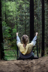 a woman on a walk in a green forest rides on a high swing attached to tall trees. the concept of active and healthy outdoor recreation