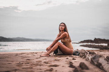 Fototapeta na wymiar Portrait of a brunette woman wearing a swimsuit on the beach in summer, sitting on the sand