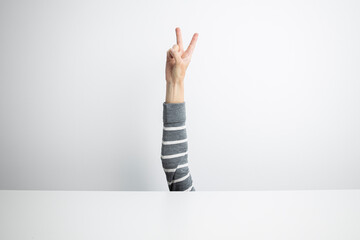 Female hand showing a gesture of victory and peace from under a white background on a white...