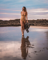 Fototapeta na wymiar A brunette woman with a swimsuit and a pareo walking along the beach in summer in the cloudy sunset
