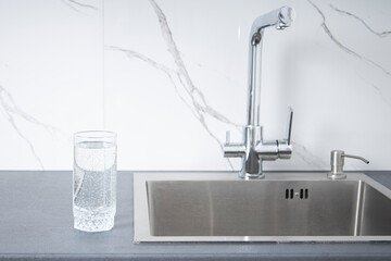 Glass of water stands on the countertop near the sink in the kitchen