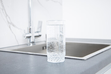 Glass of water stands on the countertop near the sink in the kitchen