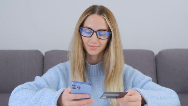Woman buying online with a credit card. Blonde female person in glasses making a mobile payment 