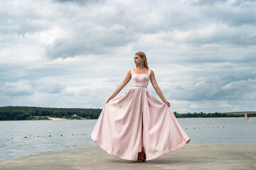 Fototapeta na wymiar Pretty young woman wear in pink fashion evening dress posing near lake in the park