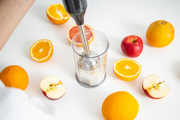 Black electric hand blender and accessories with sliced fruits on a white background. Top view, flat lay