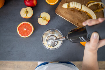Female hands holding a hand blender for mixing fresh fruit smoothies in the kitchen. Top view, flat lay