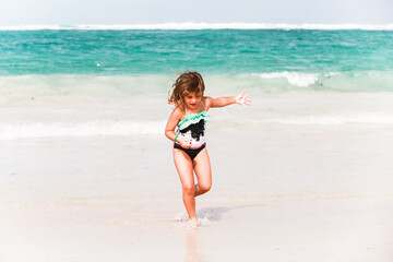 Happy little girl rinning over shore water at the beach