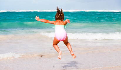 Happy little girl jumps in shore water at Bavaro beach