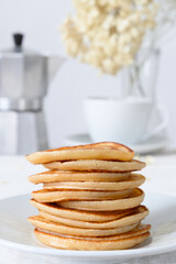 Pancakes on white plate, teacup and coffee maker on white table
