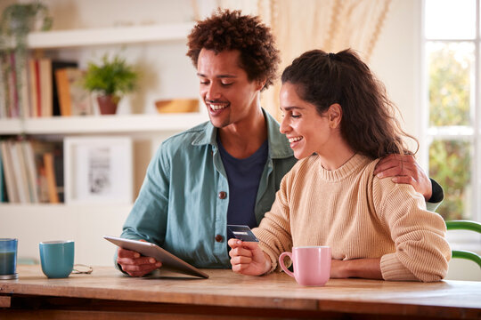 Couple With Credit Card At Home Use Digital Tablet To Review Finances For Starting Business