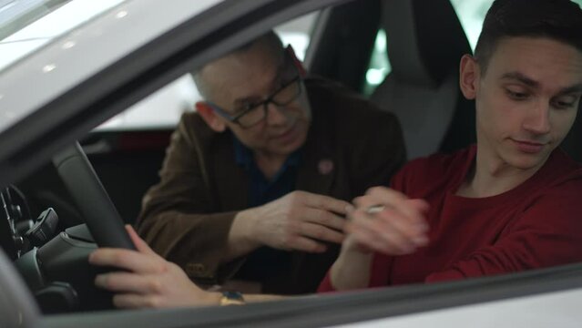 Father, son sit inside new car and fasten seat belt during test drive in modern company spbd. 4k Close view of young guy, old man test vehicles and talk with smiles, use seat belts and have good time