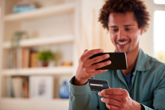 Man With Credit Card At Home Using Mobile Phone To Review Finances For Starting Business