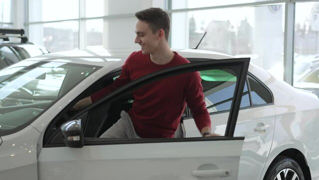 Son, father are sitting inside new car and testing while shopping in dealership office spbd. 4k Close view of young guy sits into auto and talks to older man, holds steering wheel and wants to do test