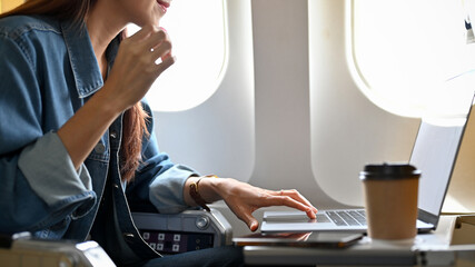 Attractive young asian female remote working on the plane, using portable laptop