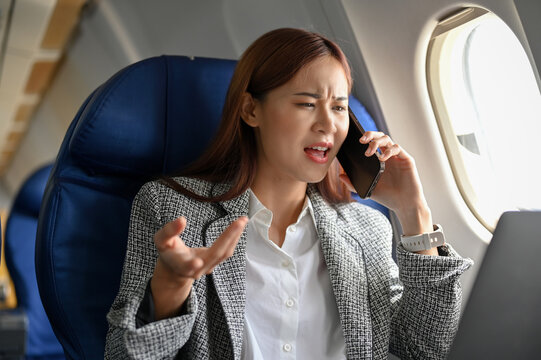 Angry asian businesswoman on the airplane, arguing and complaining problems on the phone