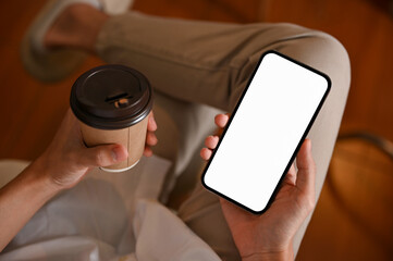 Close-up, Relaxed man sits on the chair using a smartphone and holding a cup of coffee.