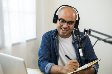 Content creator asia man host streaming his a podcast on laptop with headphones and condenser...