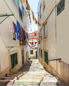 The young man sits on the steps of a staircase on a narrow old street in Alfama. Lisbon, Portugal
