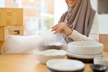 Beautiful muslim female small e-commerce business owner packing her kitchenware product