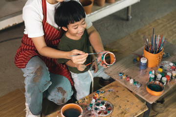 Happy family moment Mother teaching son how to painting mug cup ceramic workshop. Child creative activities and art. Kid playing pottery workshop. Developing children's learning skills.