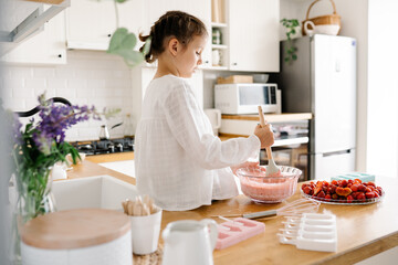Homemade ice cream. Cute little girl preparing homemade strawberry ice cream at the kitchen. Summer...
