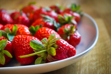 Strawberries on plate, wooden table - close-up, defocused background.