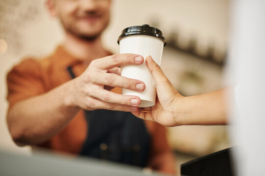 Closeup image of barista giving take-out coffee to customer