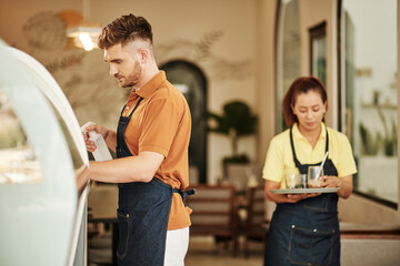 Waiter carrying tray with dirty glasses in kitchen when barista cleaning counter