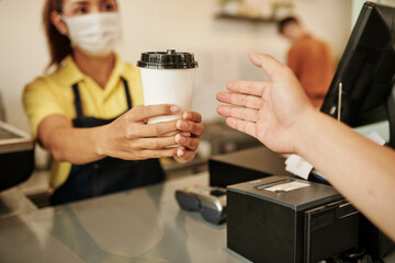Coffeeshop barista wearing medical mask when selling cup of take out coffee to customer