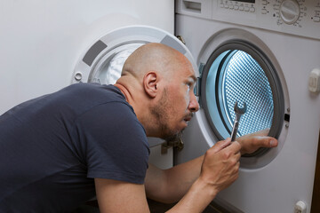 A bald caucasian man holding wrench and tried to fixed washing machine.