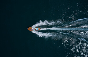 Modern wooden boat in a classic design, moving on water, aerial view. Luxurious wooden boat with people moves on dark water top view. Italian classic wooden boat fast movement on the water top view. - obrazy, fototapety, plakaty