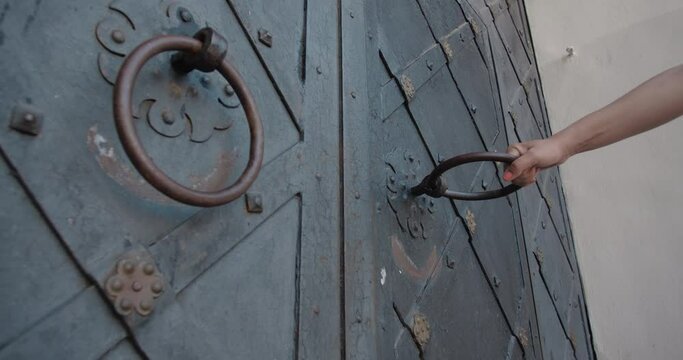 Women's hands trying to open the wrought iron gate and pulling the handle