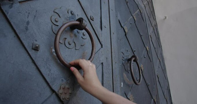 Women's hands are knocking on the closed vintage forged gates