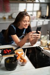 Young woman in kitchen. Beautiful woman using phone.