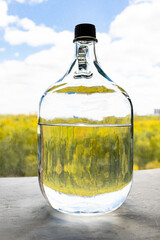 five-liter glass bottle with alcohol on concrete window sill over colorful forest on background