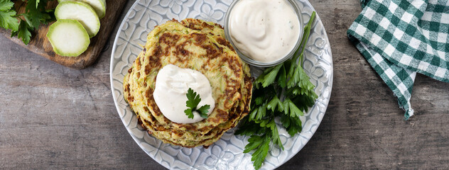 Zucchini fritters with yogurt sauce on wooden table. Panorama view