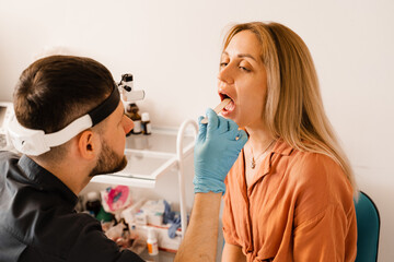 Oropharyngoscopy procedure. Otolaryngologist examines woman throat with spatula. Consultation with laryngologist.