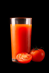 Tomato juice in a tall glass glass with natural fresh tomatoes on a black background.