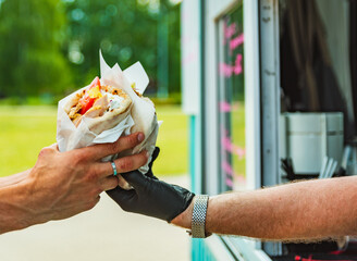 chef hands gives a gyros to man from food truck on street. street food, fast food.